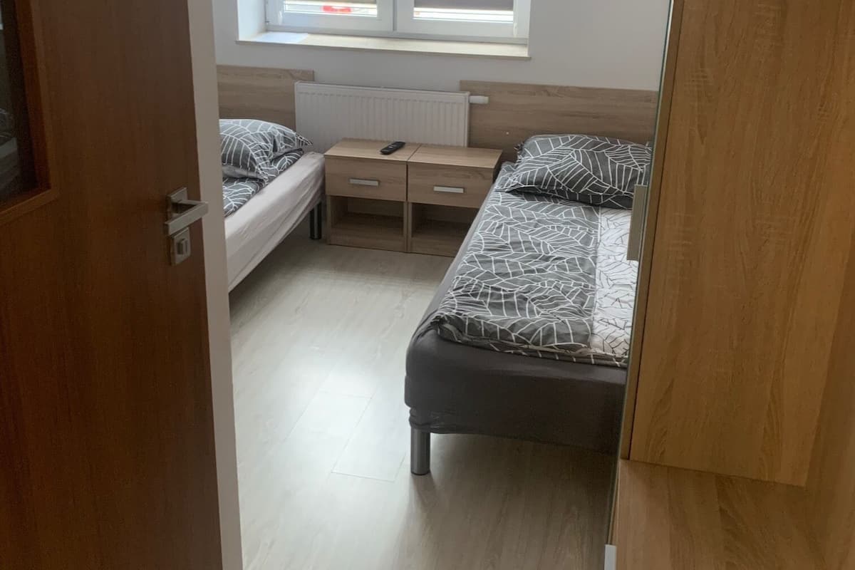 A bedroom with two beds, a window with blinds, a radiator, and a wooden wardrobe.