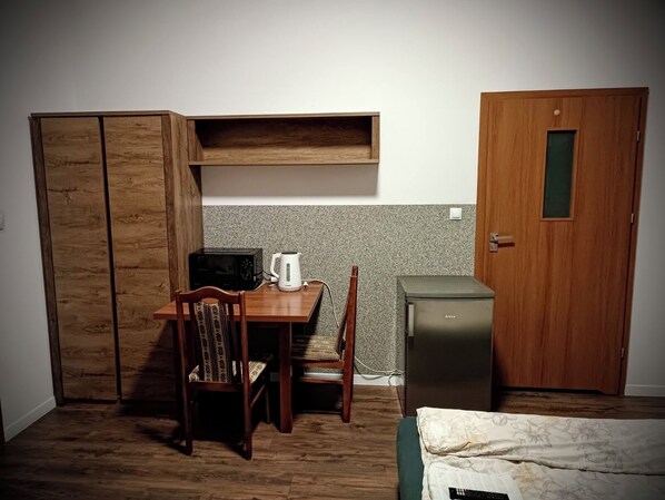 A compact room with a wooden desk, a chair, a small kitchenette, and a bed. - HOSTEL SPORTOWA (Płońsk)