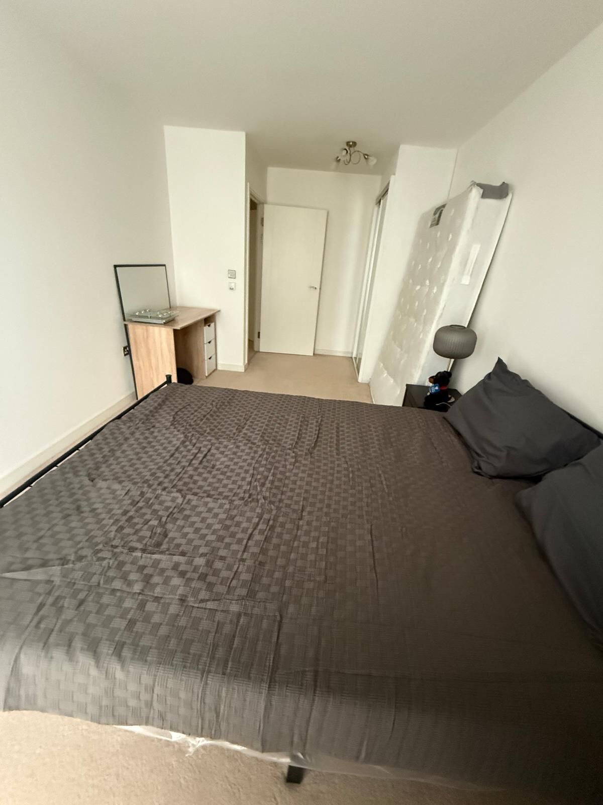 A bedroom with a large bed, a bedside table, a lamp, and a wardrobe.