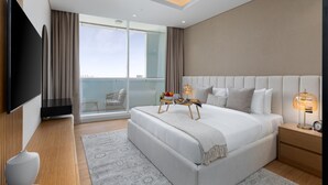 Une chambre d’hôtel moderne dotée d’un grand lit, d’un téléviseur à écran plat fixé au mur, d’une table de chevet avec une lampe et offrant une vue sur la ville grâce à de grandes fenêtres.