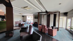 A hotel lobby with seating areas, a reception desk, and a view of the street.