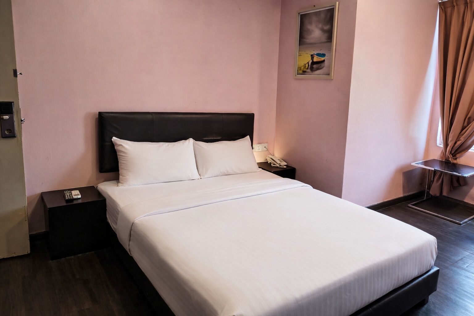 Una cama bien hecha con sábanas blancas, cabecera oscura y mesita de noche con teléfono y control remoto.
