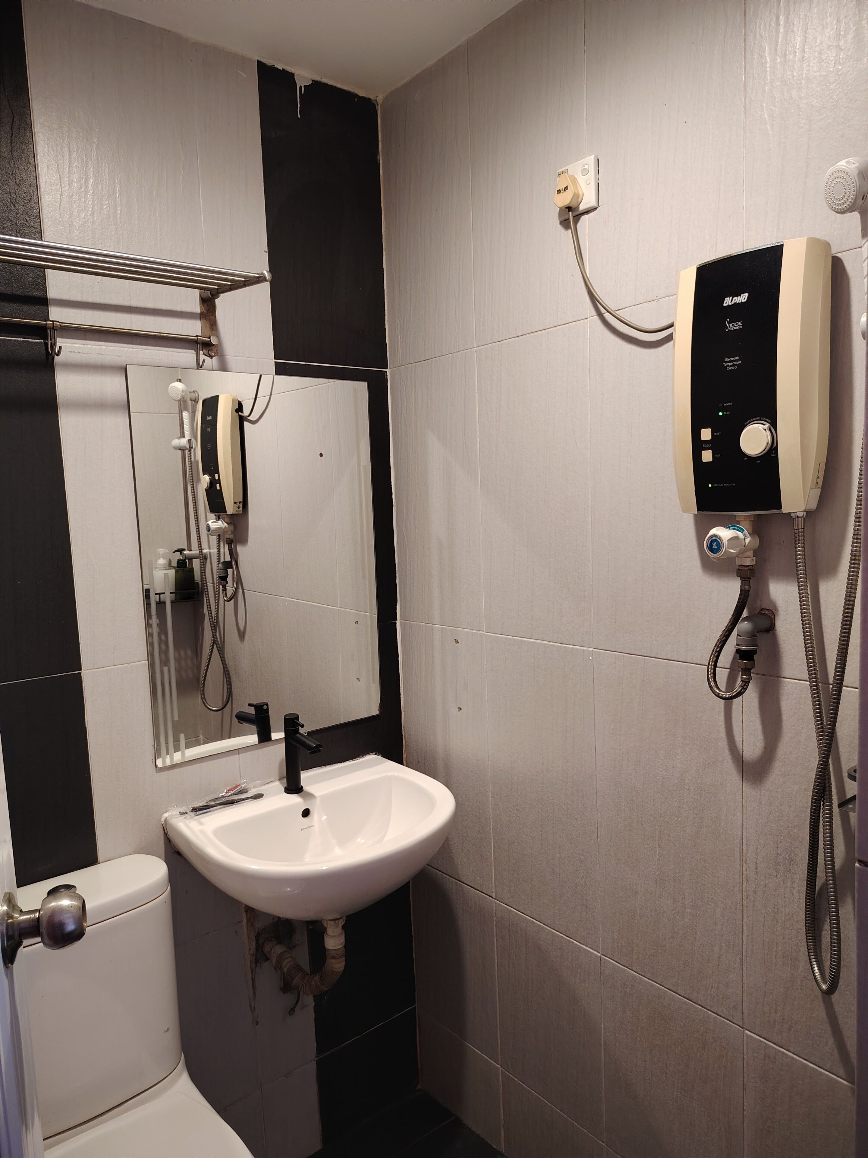 A bathroom with a white sink, a mirror, a shower, and a wall-mounted heater.