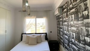 Quarto com cama, ventilador de teto, janela e parede com fotografias em preto e branco.