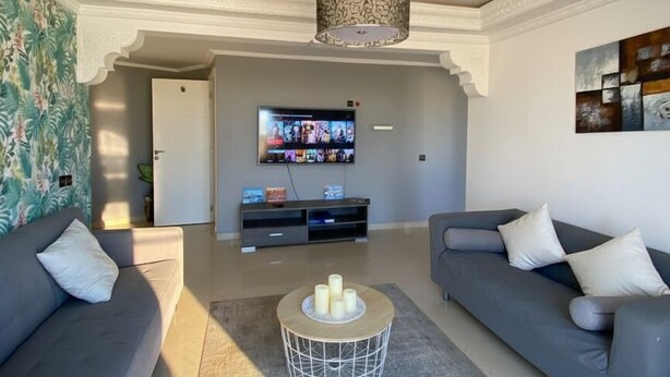 Uma sala de estar moderna com dois sofás cinzas, uma mesa de centro, uma televisão e arte decorativa na parede.