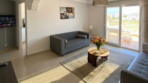 Uma sala de estar espaçosa com um sofá cinza, uma mesa de centro com flores e uma janela grande com vista para o exterior.