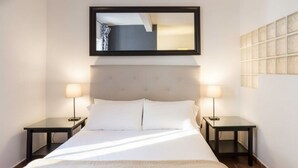 A hotel room with a large bed, two bedside tables, a headboard, and a wall-mounted mirror. - Golden Hour Studio - Steps to the Sea - A/C + WiFi (Málaga)