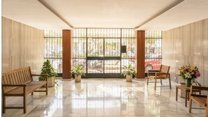 A spacious lobby with a marble floor, wooden benches, potted plants, and large windows with a view of the street. - Golden Hour Studio - Steps to the Sea - A/C + WiFi (Málaga)