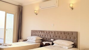 A hotel room with two beds, a large window with curtains, a ceiling fan, and wall-mounted air conditioning. - deluxe double room with mountain view (Al Haram Cairo)