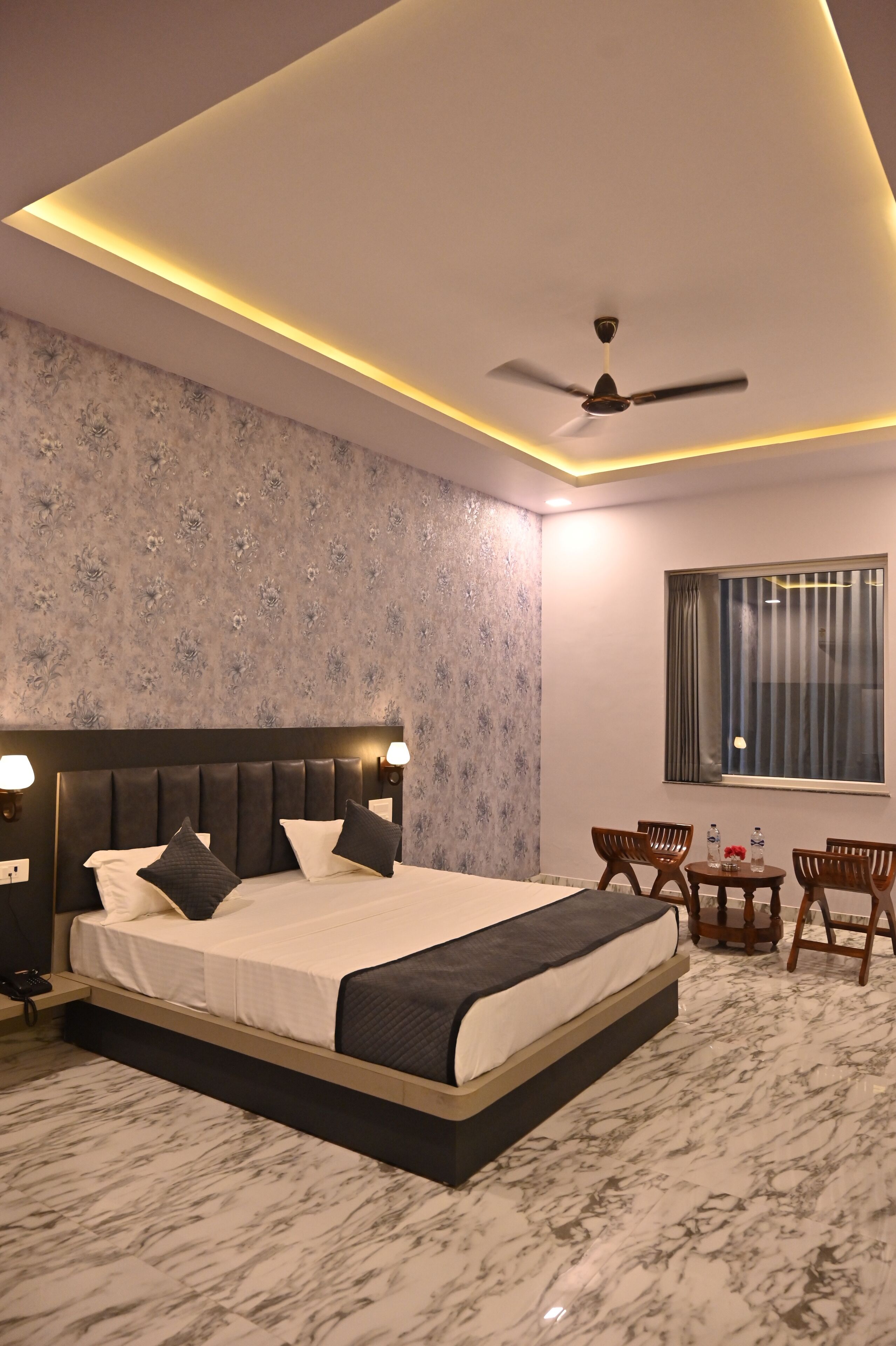 A modern bedroom with a large bed, a ceiling fan, and a small table with chairs.