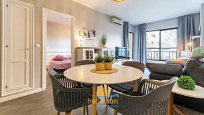 A modern living room with a round dining table, grey sofas, and a large window with curtains. - 76 – Cozy Beachfront Apartment with Pool in Fuengirola (Fuengirola)