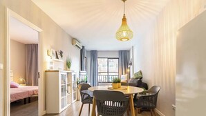 A modern living room with a dining area, a large window with curtains, and a hanging light fixture. - 76 – Cozy Beachfront Apartment with Pool in Fuengirola (Fuengirola)