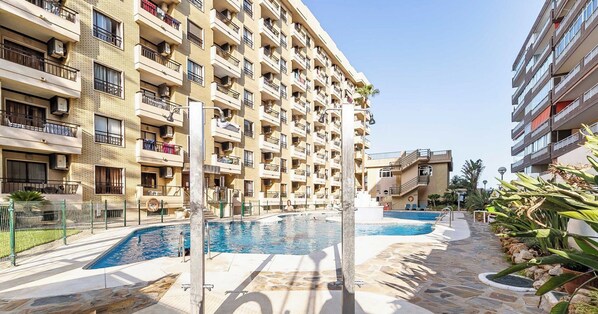 A multi-story residential building with balconies, a swimming pool, and a stone-tiled patio area.