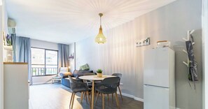 A modern kitchen with a dining area, a refrigerator, and a hanging coat rack.
