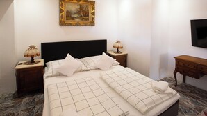 Una cama bien hecha con cabecera negra, dos lámparas de noche, un cuadro en la pared y una mesita de noche de madera.