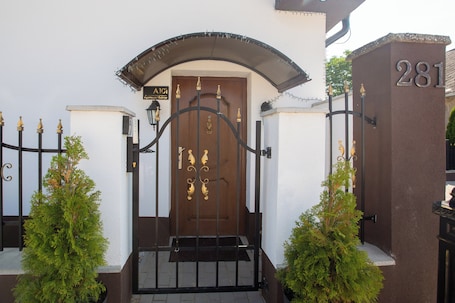 A gated entrance with a brown door, a sign above the door, and a number '281' on a wall to the right.