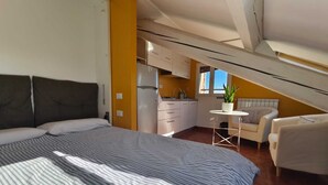 A bedroom with a large bed, a small table, a sofa, and a kitchenette in the background. - Cozy and bright loft studio apartment in Milan (NO.LO) (Milano)