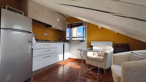 A compact kitchen with a refrigerator, stove, and white cabinets. There's a small table and a sofa in a room with a sloped ceiling and a window. - Cozy and bright loft studio apartment in Milan (NO.LO) (Milano)