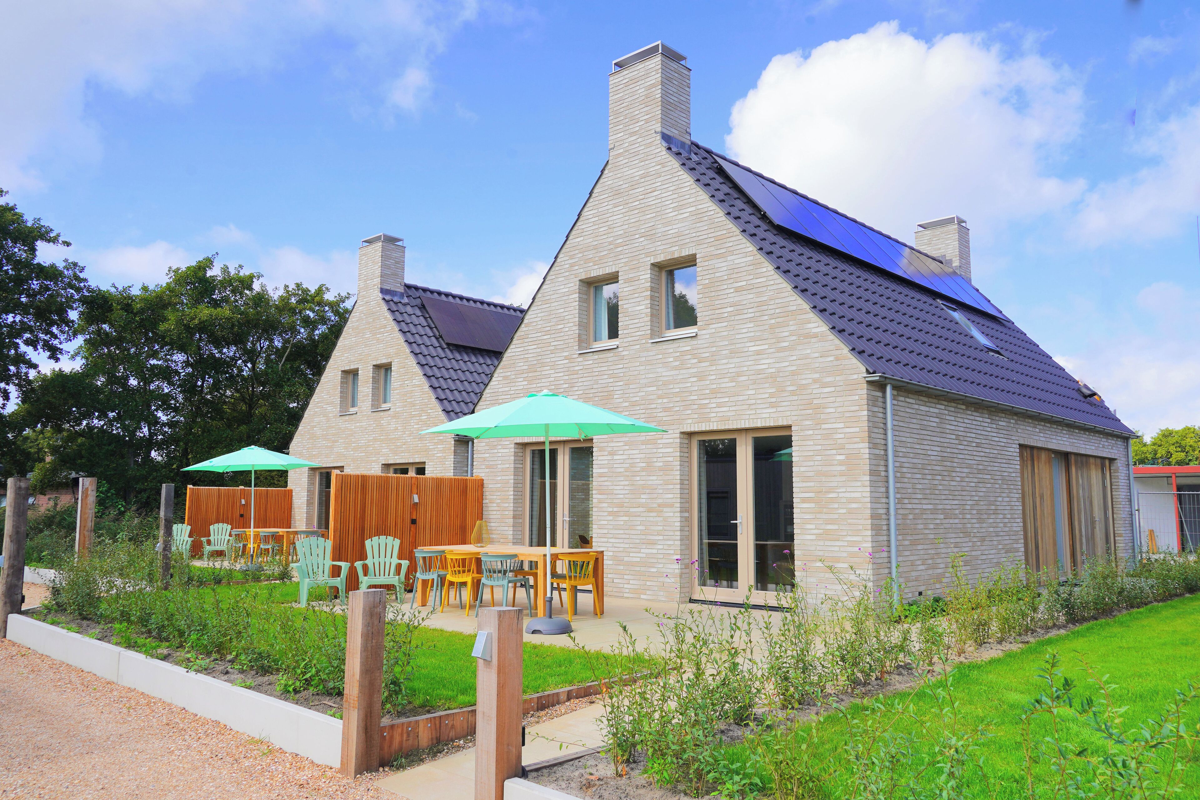 Ein zweistöckiges Haus mit geneigtem Dach, ein Garten mit Holzpforte und Außenmöbel mit Stühlen und Tisch.