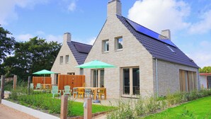 A two-story house with a sloped roof, a garden with a wooden fence, and outdoor seating with chairs and a table. - Vakantiehuis Zee - Callantsoog op zijn best! (Callantsoog)