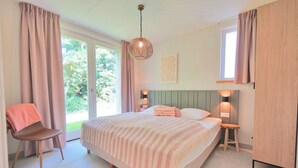 A bedroom with a bed, bedside tables, a chair, and a window with curtains. - Vakantiehuis Zee - Callantsoog op zijn best! (Callantsoog)