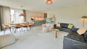A modern living room with a dining area, a kitchen in the background, and a sofa with cushions. - Vakantiehuis Zee - Callantsoog op zijn best! (Callantsoog)