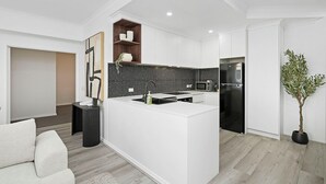 A modern kitchen with a black and white backsplash, a built-in island, and a black refrigerator. - Modern City Escape | Stylish 2BR Apartment (East Perth)
