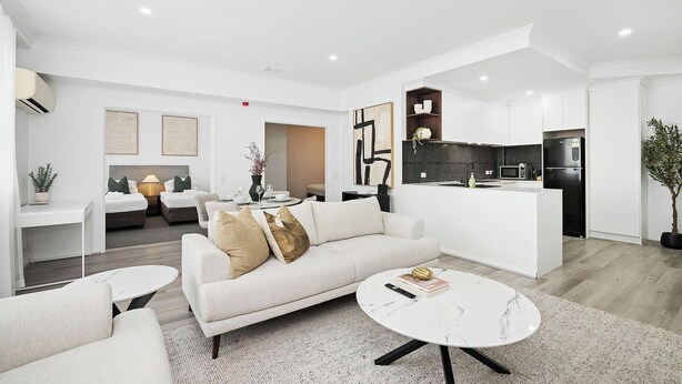 A modern living room with a sofa, coffee table, and a kitchen area with a refrigerator and microwave. - Modern City Escape | Stylish 2BR Apartment (East Perth)