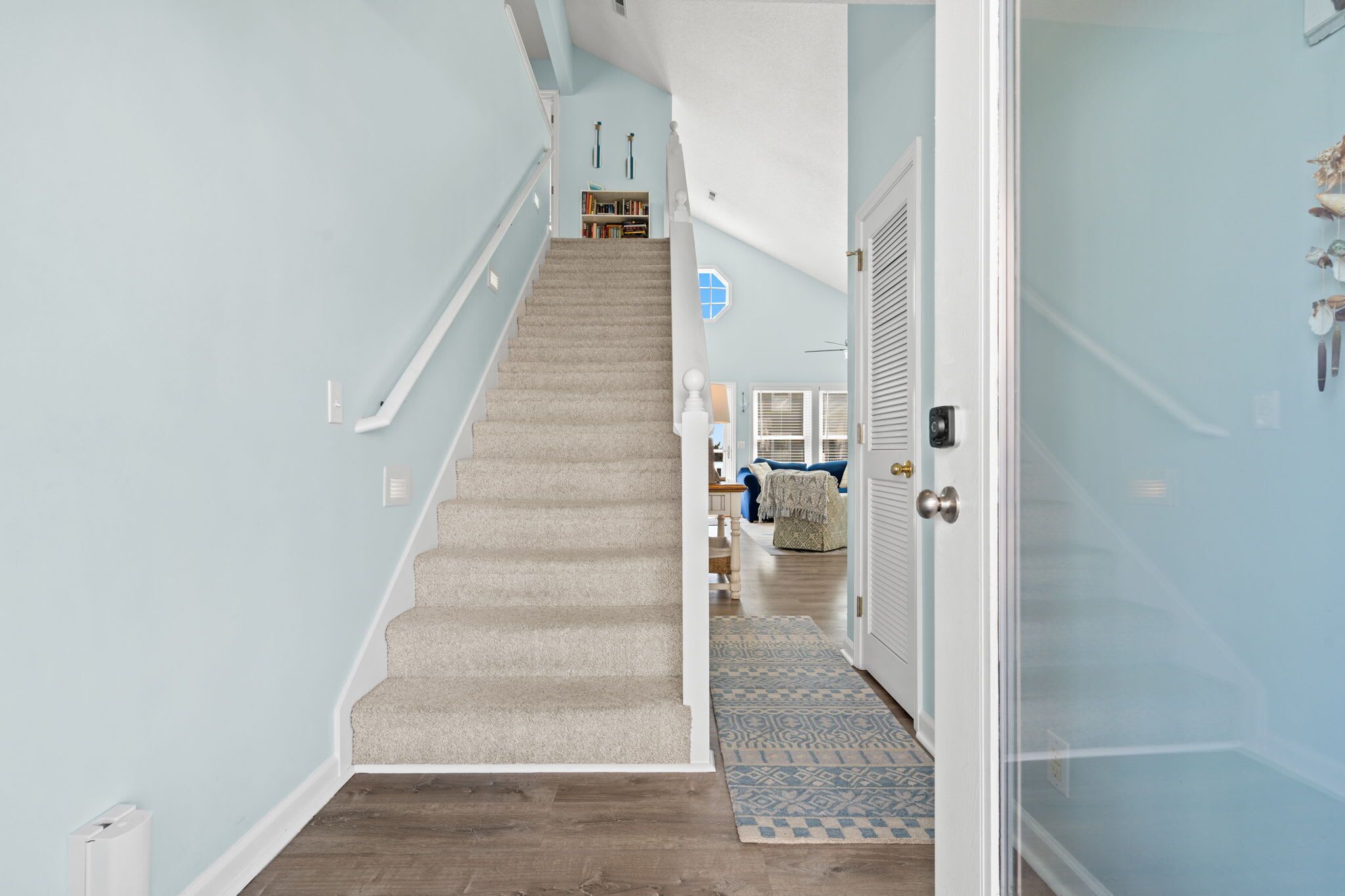 A staircase leading to a living area with a blue wall, a patterned rug, and a door with a glass panel.