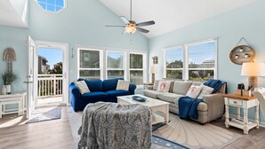 Ein geräumiges Wohnzimmer mit blauer und weißer Farbgestaltung, ausgestattet mit einem Deckenventilator, großen Fenstern und Blick ins Freie.