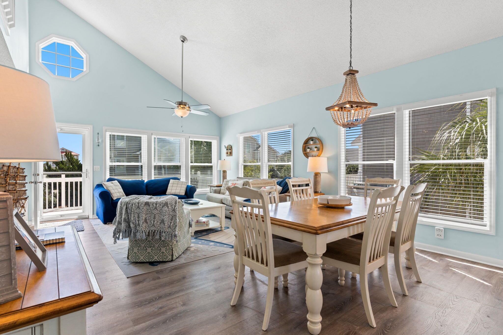 A spacious living area with a dining table, white chairs, and a ceiling fan.