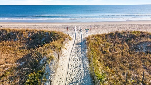 Ein Strandweg, der zum Meer führt, mit blauem Himmel.