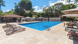 Piscina com espreguiçadeiras e guarda-sóis, cercada por palmeiras e um céu claro.