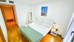 A hotel room with a bed, a nightstand with a lamp, a painting on the wall, and a wooden floor. - Bielsa del Pilar - Turistea  (Zaragoza)
