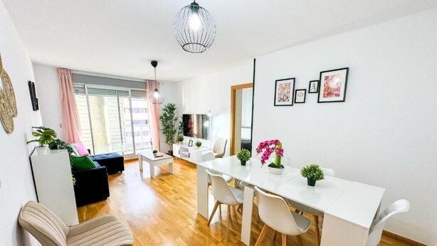 A modern living room with a dining area, wooden flooring, a white dining table, and a hanging light fixture. - Bielsa del Pilar - Turistea  (Zaragoza)