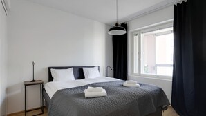 Ein modernes Hotelzimmer mit einem großen Bett, einem Nachttisch, einer Stehlampe und einem Fenster mit Vorhängen.