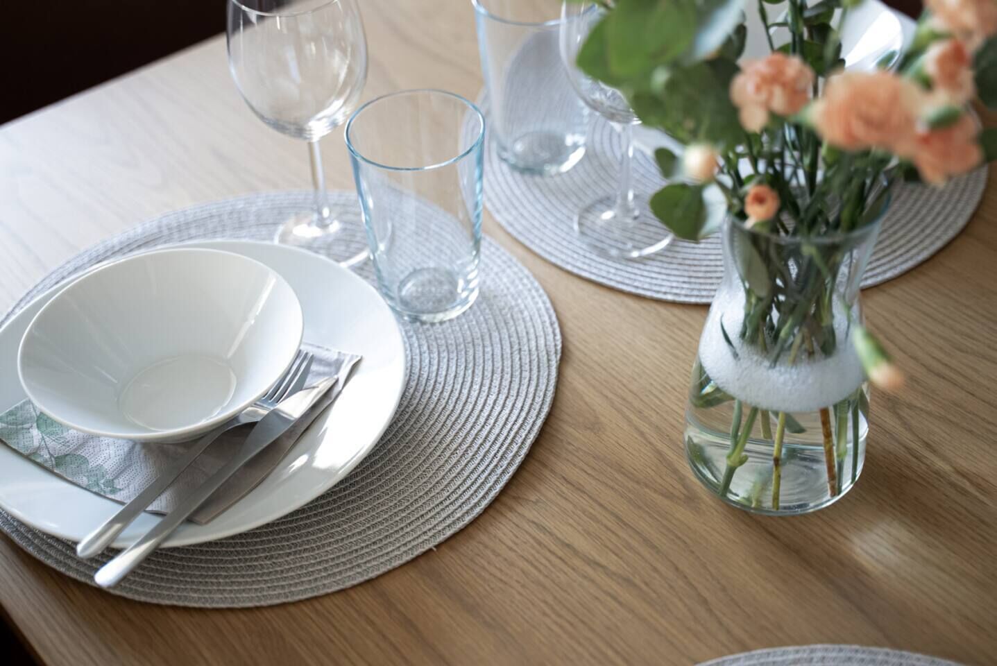 Una mesa de comedor con platos, cubiertos y un jarrón con flores.