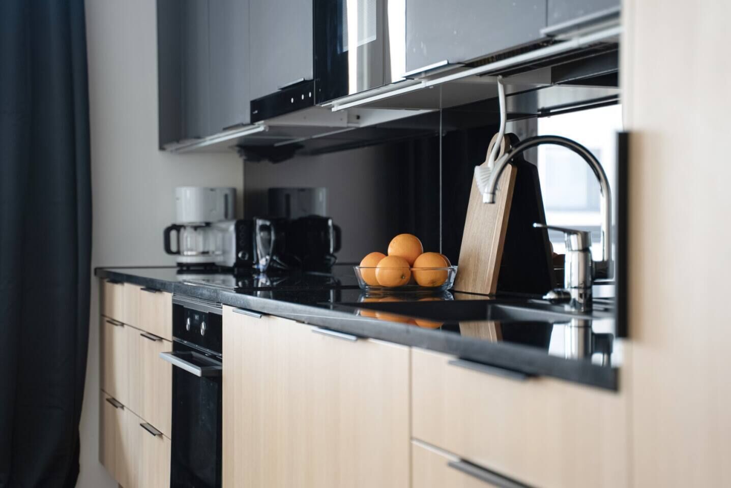 A modern kitchen with a black countertop, a coffee maker, and a bowl of oranges.