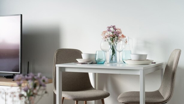 Een eettafel met stoelen, een vaas met bloemen en een televisie op een meubel.