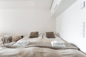 Une chambre à coucher avec un lit, des oreillers, une table de chevet et un luminaire fixé au mur.