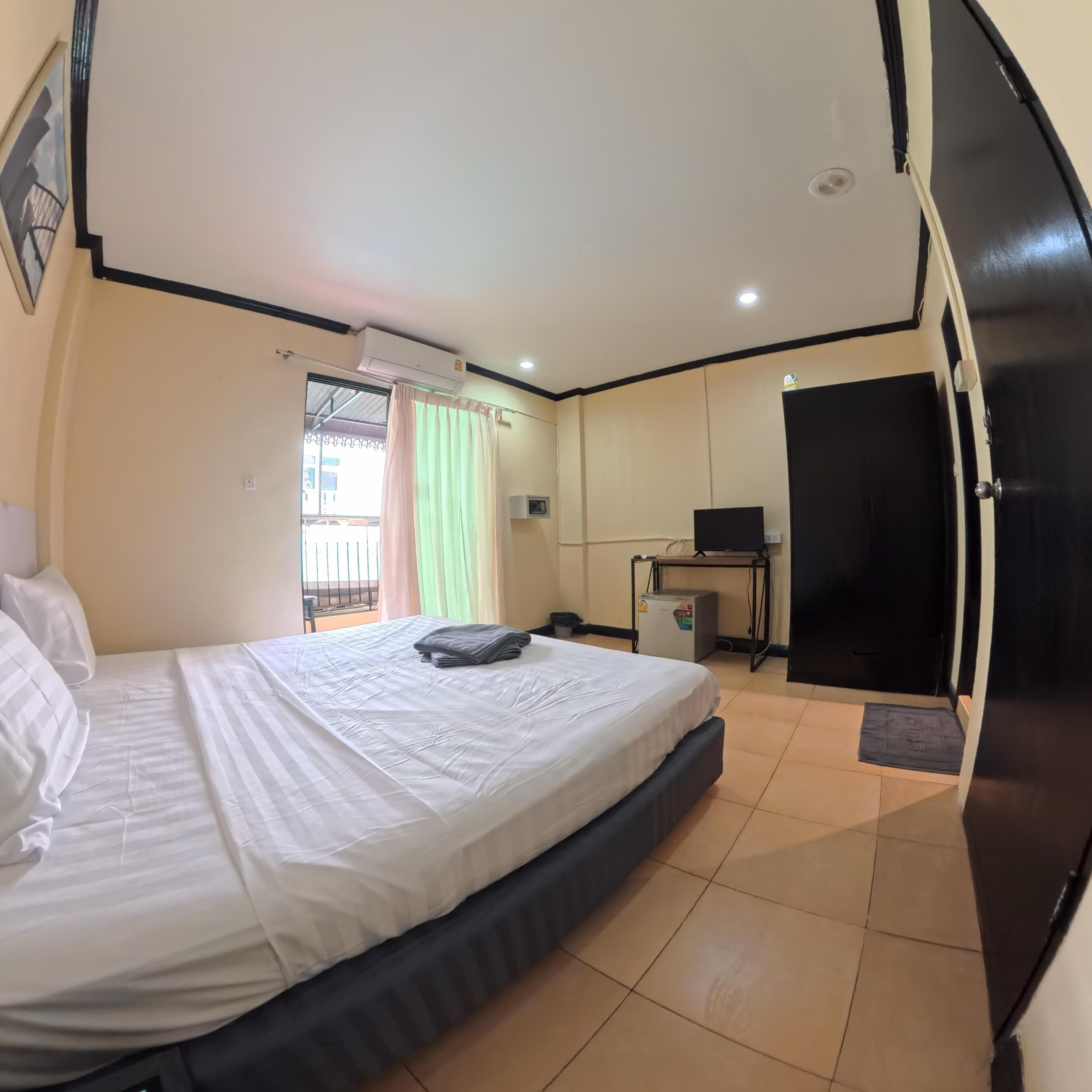 A hotel room with a bed, a desk, an air conditioning unit, and a door.