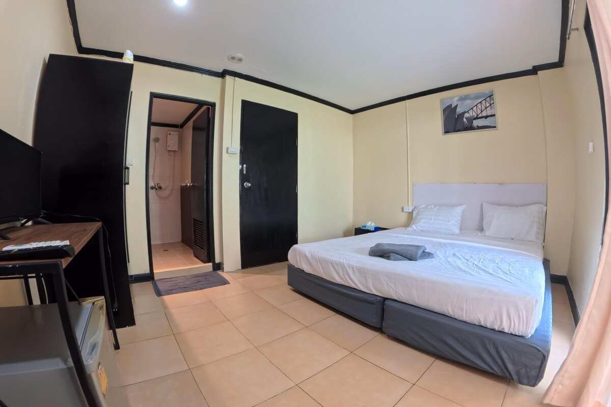 A hotel room with a bed, a desk, a TV, and a shower area.