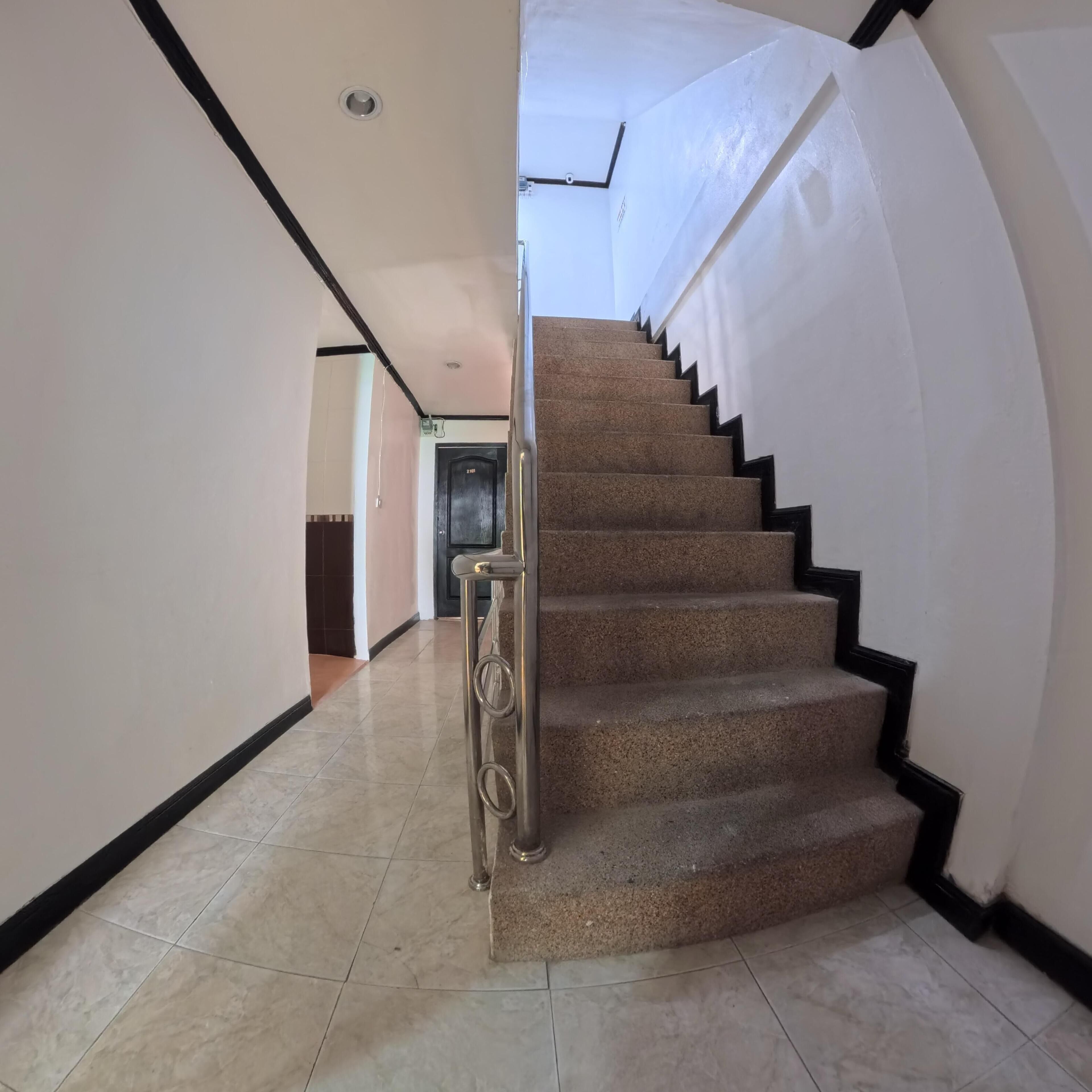A staircase with a handrail, leading to a landing with a door. The walls are plain, and the floor is tiled.