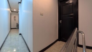 A hallway with a black door, white walls, and a tiled floor. - Stay 94 Patong (Patong)