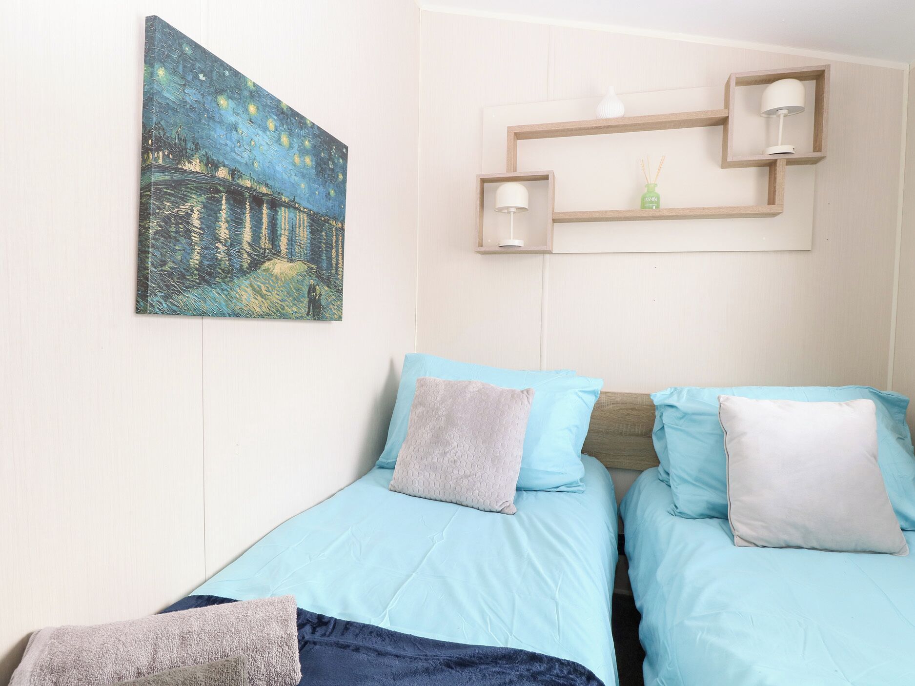 A bedroom with two beds, a night sky painting, and a shelf with two lamps and a bottle.