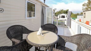 Un patio con muebles de mimbre, una pequeña mesa redonda, una estatua de perro blanco y una puerta blanca que da a una zona cubierta.