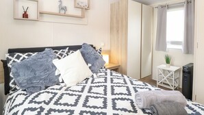 Un dormitorio con cama, mesita de noche, calefactor y ventana con cortinas.