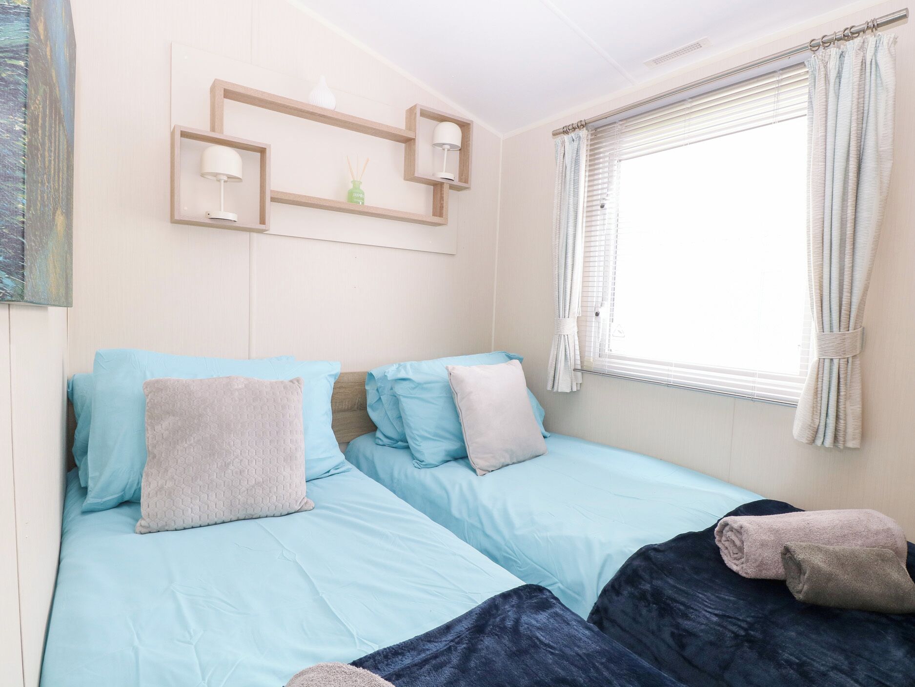 Un dormitorio con dos camas, una ventana con cortinas y una estantería con lámparas.