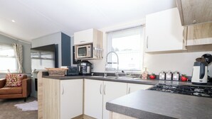 Cocina compacta con microondas, estufa y lavamanos. Tiene una pequeña zona de comedor con sofá y ventana.