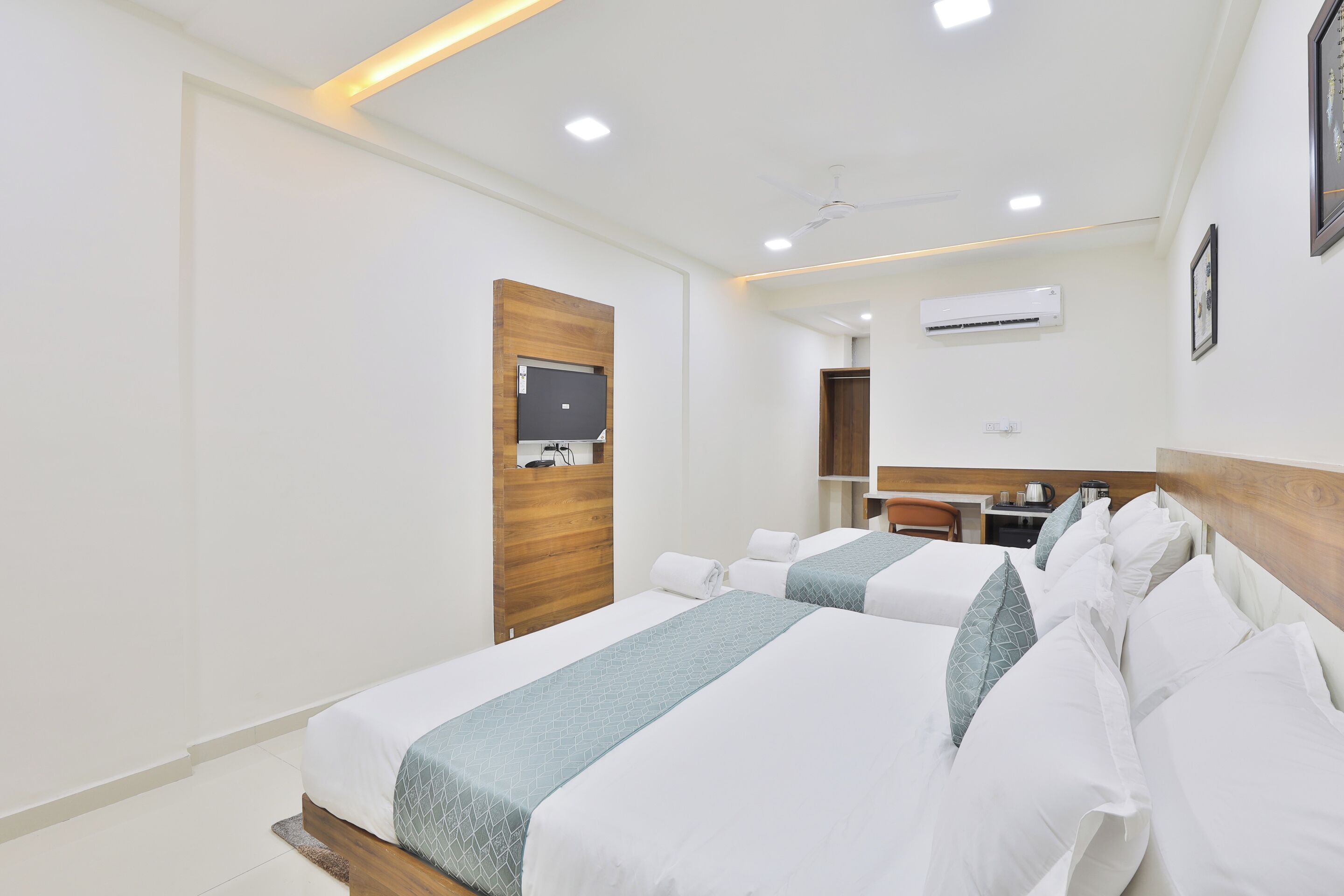 A hotel room with two beds, a wooden headboard, a flat-screen TV, an air conditioning unit, and a small desk with a chair.